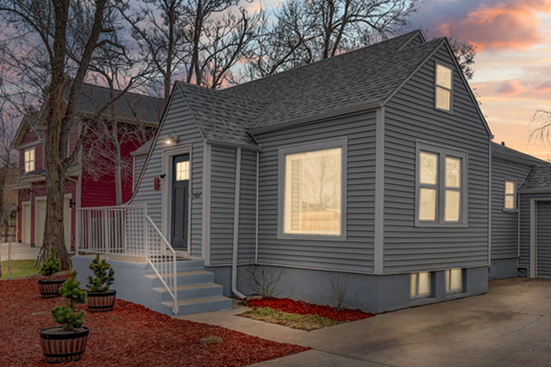 A gray house with a red mulch yard sits beside a red house with a gray roof.