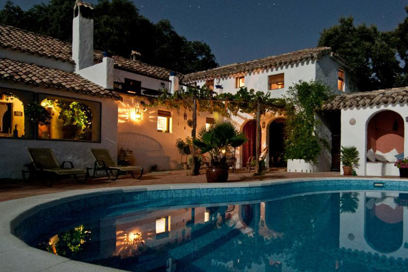 A large pool reflects the lights of a gorgeous property at night.