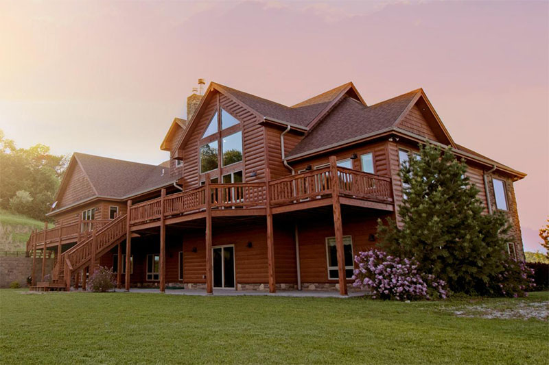 A house with a sleek log cabin look sits atop a patch of green grass.
